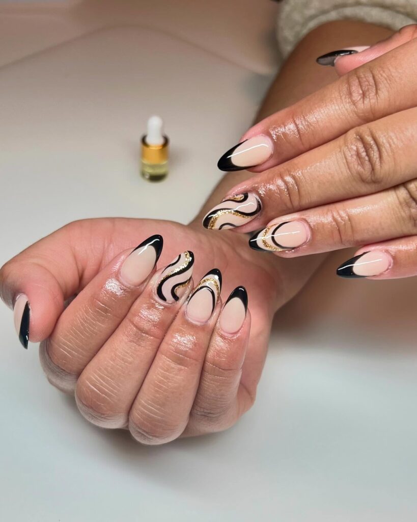 Almond Nails with Nude Base and Black French Tips Paired with Gold Sparkling Waves for a Chic Graduation Statement