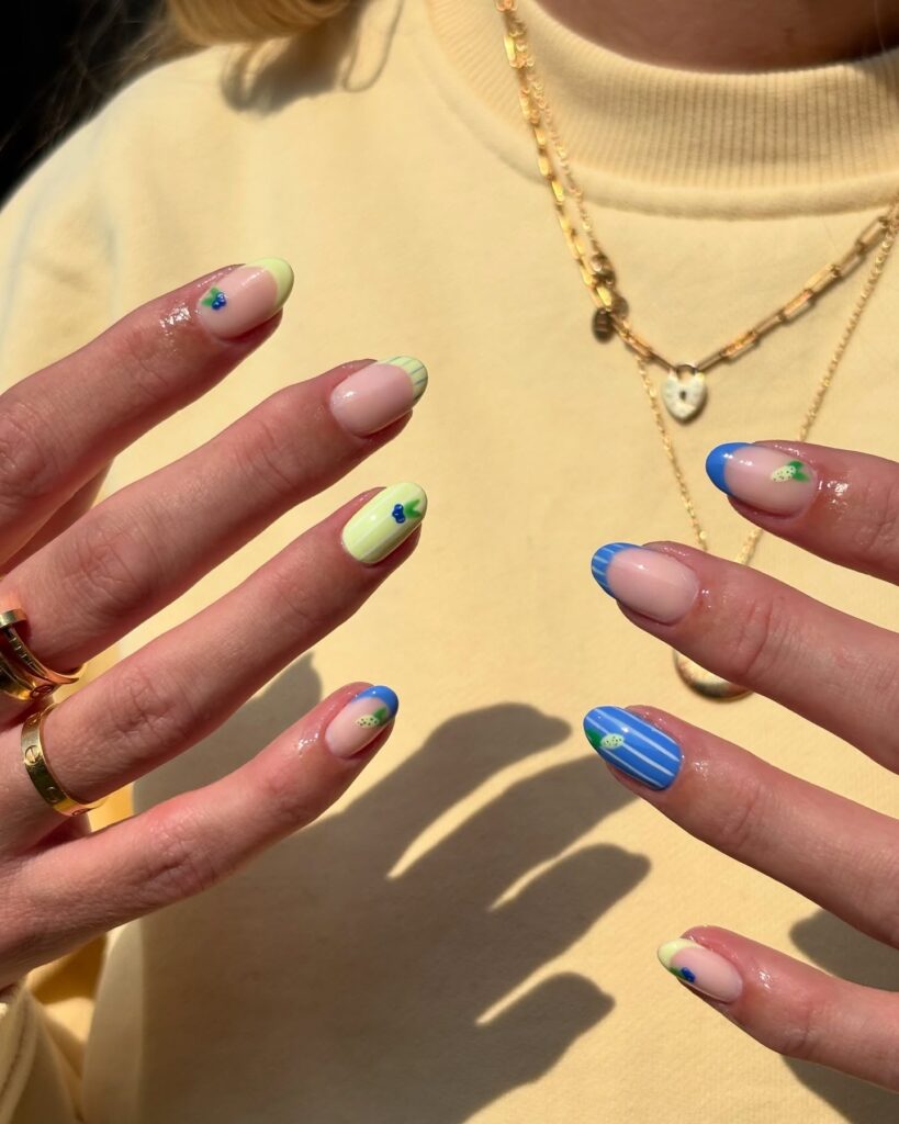 Almond nails with pastel yellow and sky blue tips featuring floral and fruit accents for a garden inspired spring look