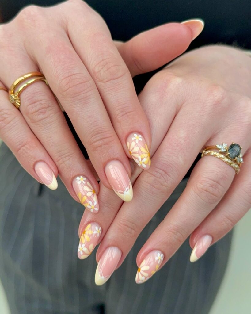 Almond nude nails with yellow French tips and daisy art for a playful and cheerful spring floral design