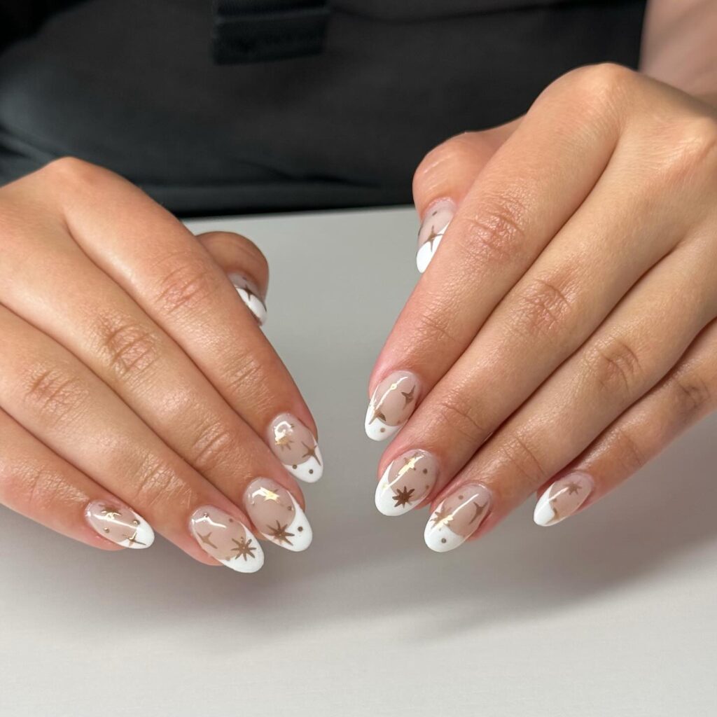 Elegant Almond Nails with Sheer Nude Base, White French Tips, and Gold Celestial Starbursts for a Magical Graduation Theme
