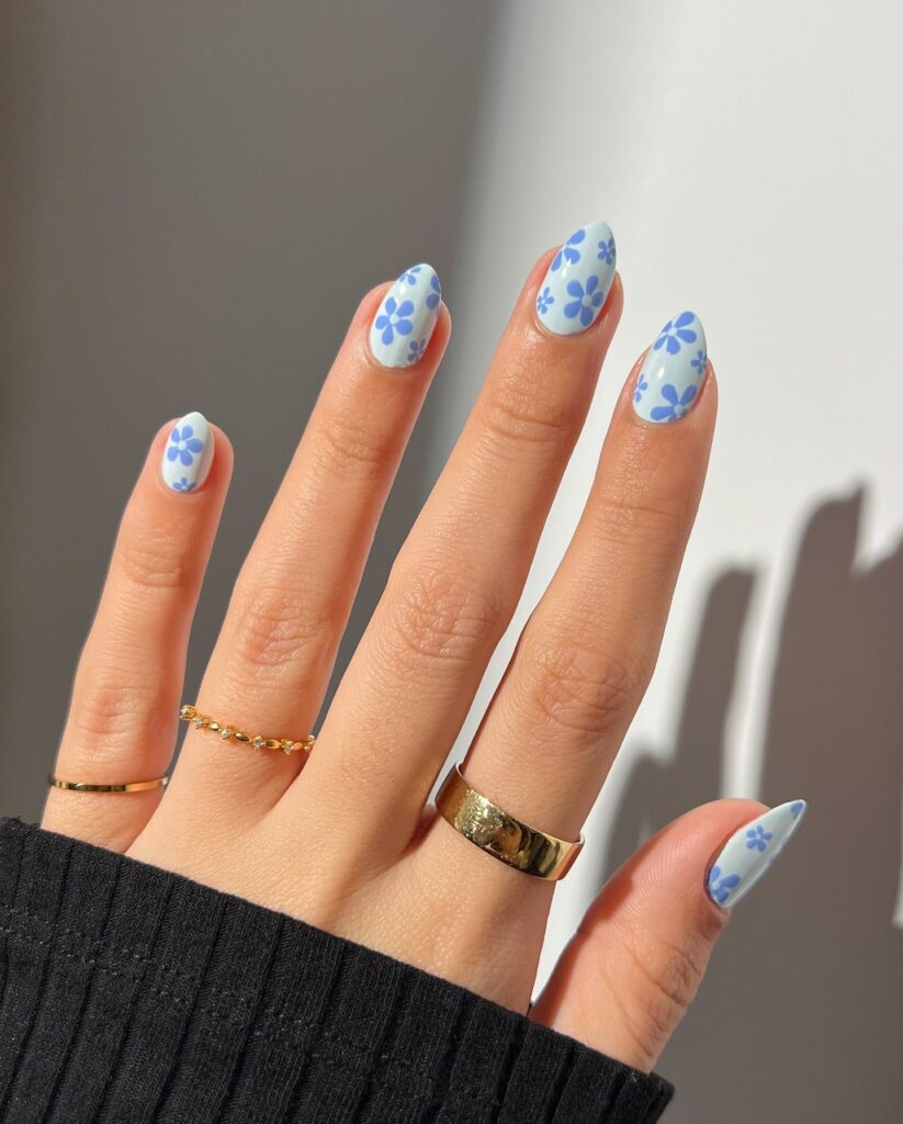 Pastel baby blue almond nails with medium floral artwork for a charming and retro inspired spring nail design