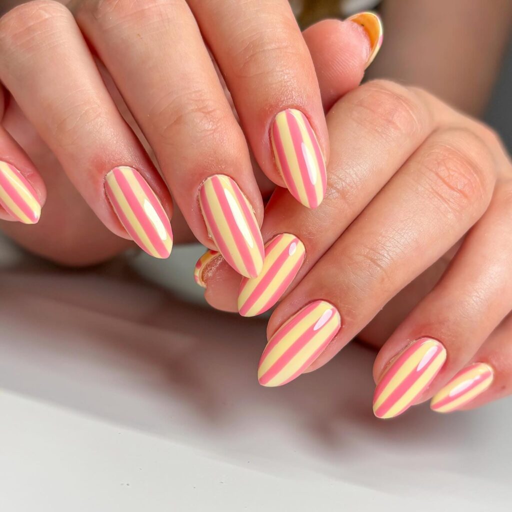 Pastel yellow and pink striped almond nails for a playful summer nail art idea with candy colors