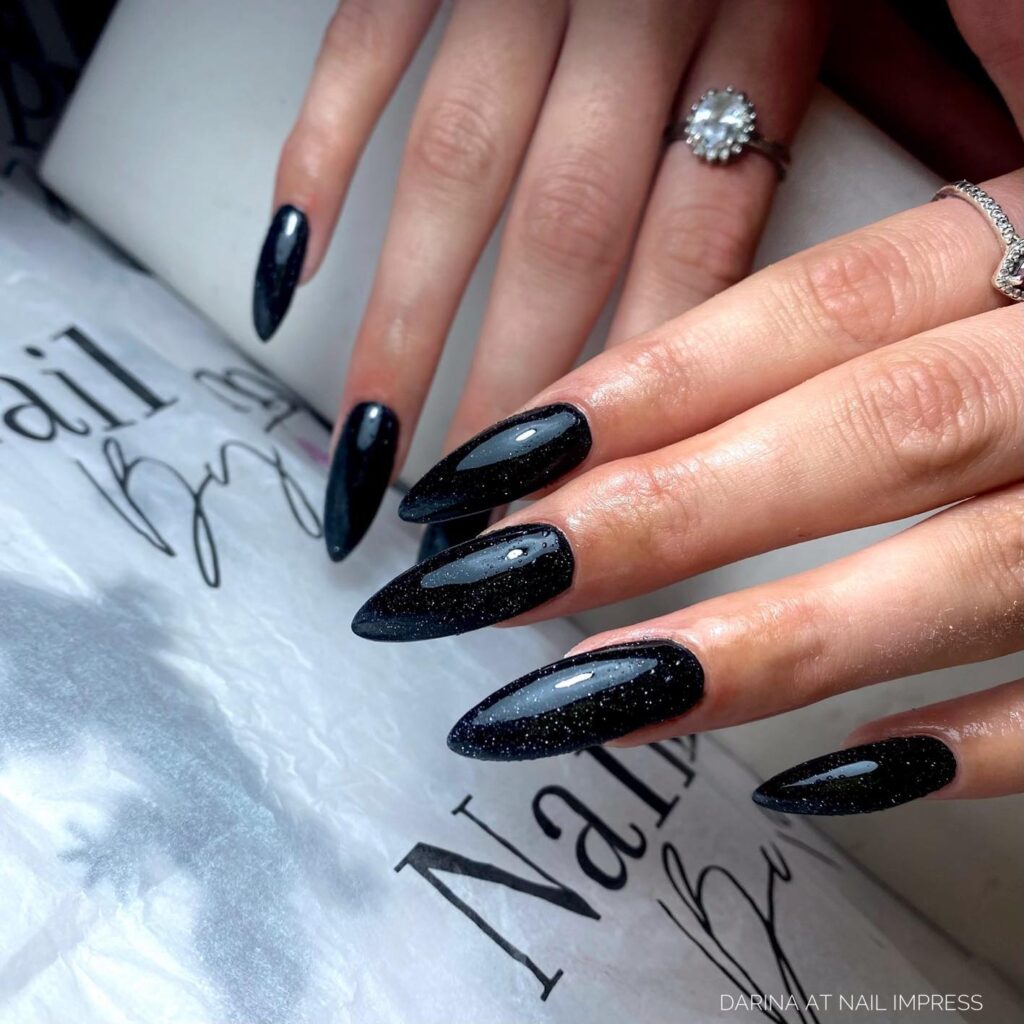 Almond shaped black glitter galaxy nails for a glamorous night sky manicure perfect for evening events
