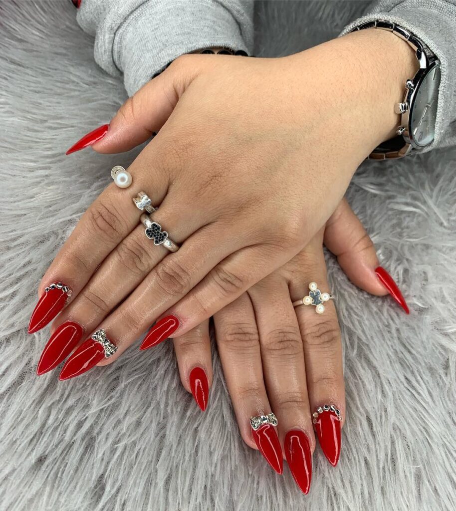 Bold Stiletto Red Nails with Rhinestones and Metallic Bow Embellishments