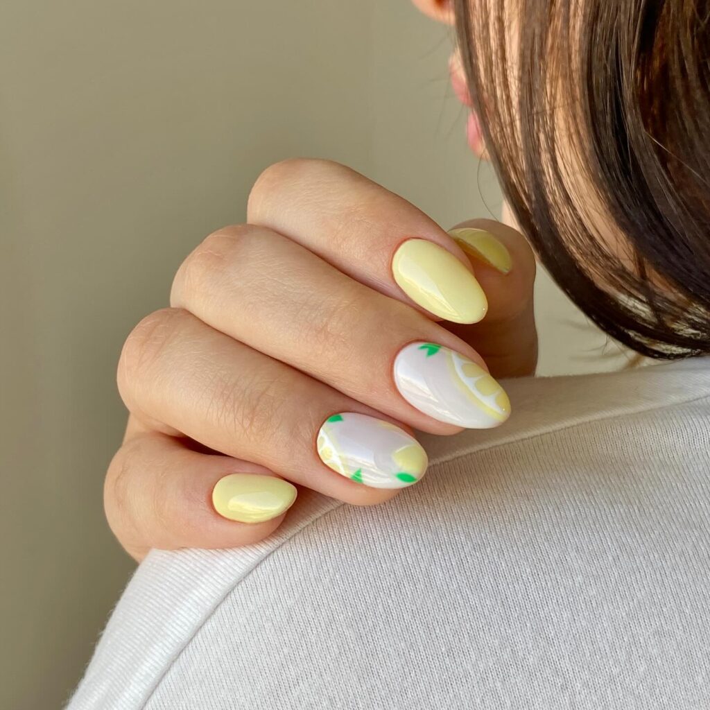 Pastel yellow lemon short nails with white accents and tiny green leaves for bright summer fruit nail art