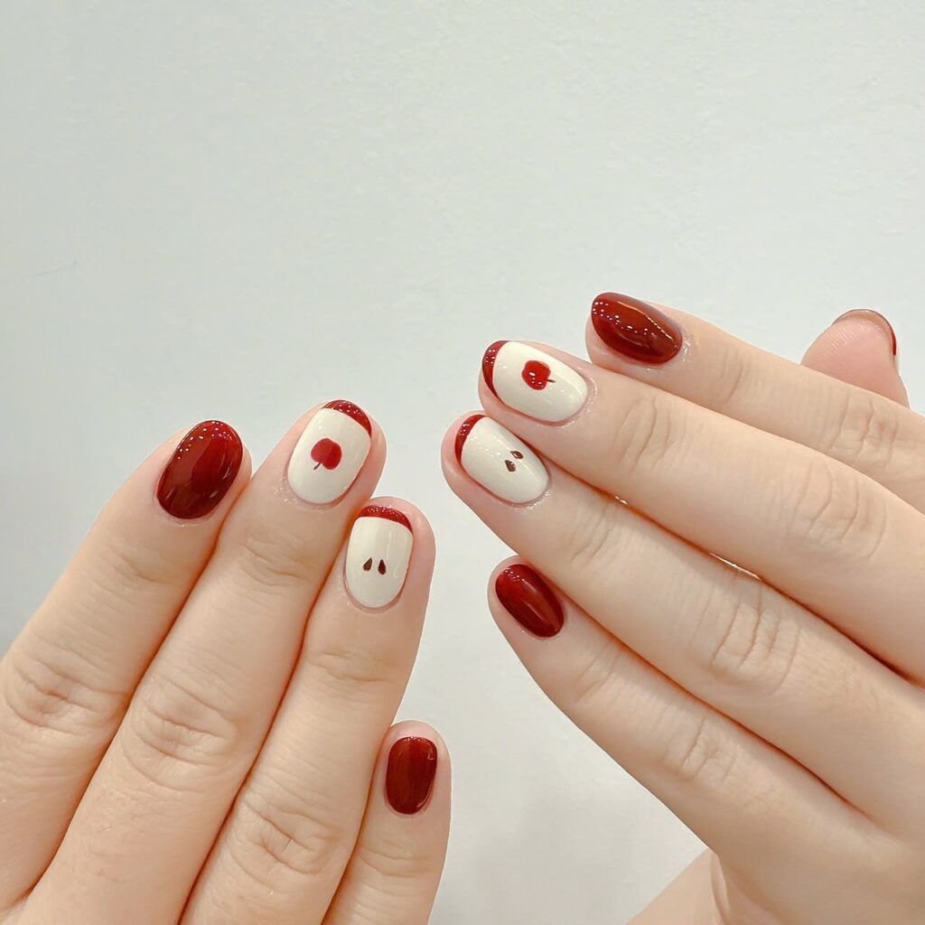 Red apple nail art on short rounded nails with creamy nude base and minimalist fruit details